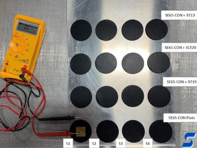 Grid of conductive material cut in circles shown with contacts of measuring device attached to front left